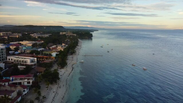 Alona Beach, Panglao, Bohol, Philippines: may 2022 - Sunset scene at the beach lined with outdoor bars and restaurants, and tourists walking by the shore.