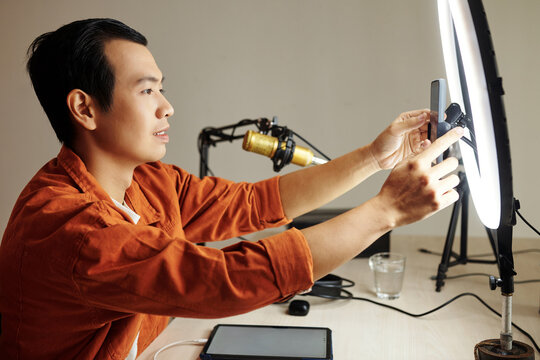 Blogger setting smartphone on monopod with ring light to film video for social media