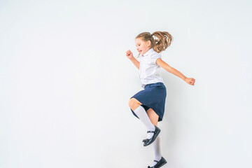 happy schoolgirl in a school uniform, jumping on a white background in the studio. the little girl is ready for school conceptual school. the holidays begin. Advertising discounts