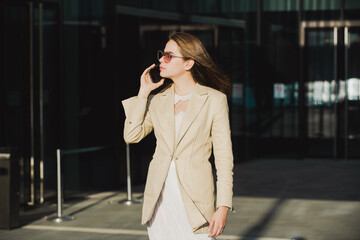 Fototapeta premium Beautiful business woman in fashionable summer spring clothes outdoors talking on phone outdoor. Female stylish model walking city street. Summer trend, fashion outfit.