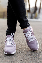 Fototapeta na wymiar cropped image of female legs in shoes. Woman in black jeans and pink sneakers stands on pavement