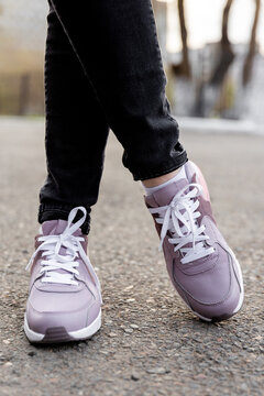 cropped image of female legs in shoes. Woman in black jeans and pink sneakers stands on pavement