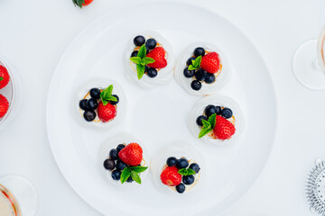 Top view meringue dessert Pavlova cakes with fresh cream, strawberries and blueberries, decorated with mint on the white plate. Recipes for delicious light desserts. Summer cafe menu. Selective focus.