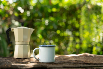 Hot coffee in a white enamel mug on an old wooden floor while camping in the forest. soft focus.shallow focus effect.