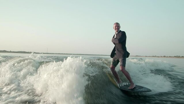 A surfer jumping on a wakeboard in a suit. An experienced wakeboarder sprays water drops into the camera.