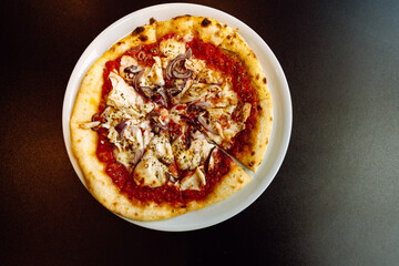 Top view of a pizza with chicken and red onions on a plate on a black table