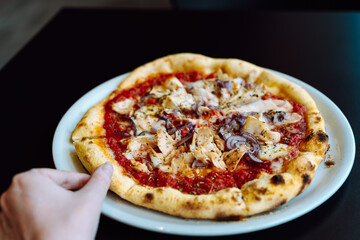 Hand takes a slice of pizza with chicken from a plate