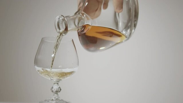 Golden whiskey, cognac pouring in the glass from the bottle.  Cognac is poured into a glass. white background