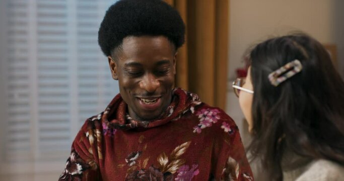 Christmas party. An African-looking guy gets present. The Asian-looking girl presented gift and hopes the guy will like it. The guy is pleasantly surprised and very happy with the gift.
