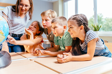 A group of pupils children with teacher together in class, learning. School teacher and children using globe. Geography worldwide explorer continent country concept.