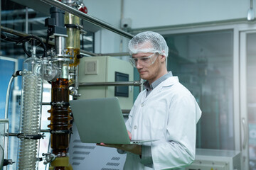 Scientist holding laptop and controlling rotational vaporizer during oil extraction. hemp oil extraction process.