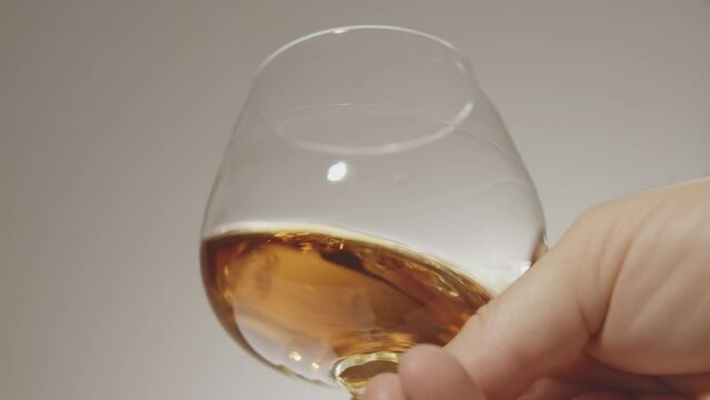 Close up shot of a p  cognac glass in hand. slow motion. white background. A lonely man drinks liquid
