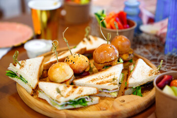 sandwiches and mini burgers on a wooden tray. 