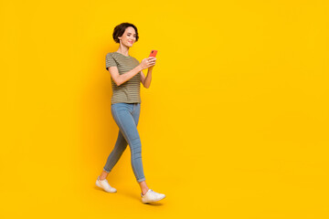 Photo of dreamy cute girl dressed green t-shirt typing modern gadget walking empty space isolated yellow color background
