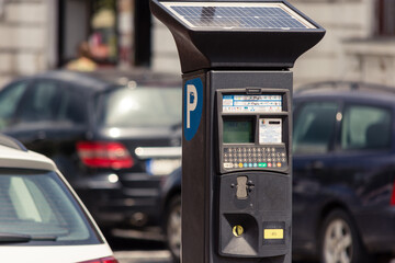 Parking meter with solar panel for renewable energy in parking lot with cars around it