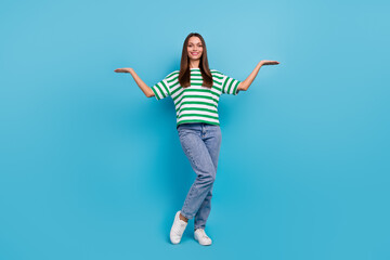 Fototapeta na wymiar Full size photo of optimistic young lady hold empty space wear t-shirt jeans shoes isolated on blue color background