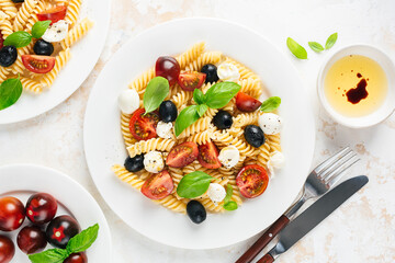 Cold pasta salad with fussili, cherry tomatoes, mozzarella cheese and olives on a plate, top view