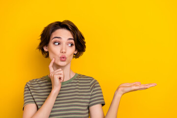 Photo of young funny girl touch cheek holding hand promote new deal product shop looking empty space isolated on yellow color background