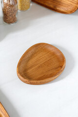 Empty wooden plate on kitchen white table. Wooden oak little dish, board, tray. Empty and template mockup with place for food. Kitchen utensils.