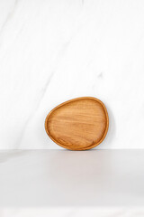 Wooden little oak dish, board, tray standing near the wall. Empty wooden plate on kitchen white table. Empty and template mockup with place for food. Kitchen utensils.