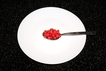 Red berries in a spoon on a white plate. Fresh red currant. Dark table.