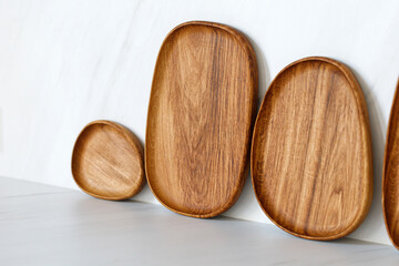 Wooden oval oak dishes, boards, trays standing near the wall. Empty wooden plates on kitchen white table. Kitchen utensils.