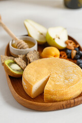 French Reblochon cheese on wooden plate with fruits and honey. Cheese plate, dish. Cutting cheese.