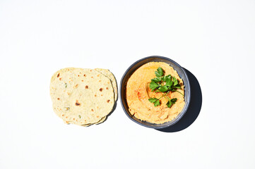 Flat lay with pita bread and a bowl of chickpea hummus sprinkled with paprika and parsley isolated on white background