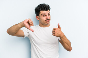 Young caucasian man isolated on blue background showing thumbs up and thumbs down, difficult choose...