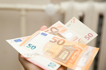 Heating thermostat with money. Expensive heating costs concept. Payment for warm house in winter. Energy and heating cost waste theme. Central heating. House renovation concept.