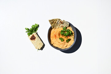 Flat lay. Blue ceramic bowl with chickpea hummus sprinkled with red chili and parsley wrapped in pita bread. Still life