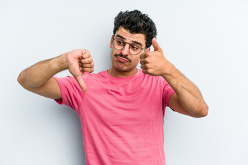 Young caucasian man isolated on blue background showing thumbs up and thumbs down, difficult choose...