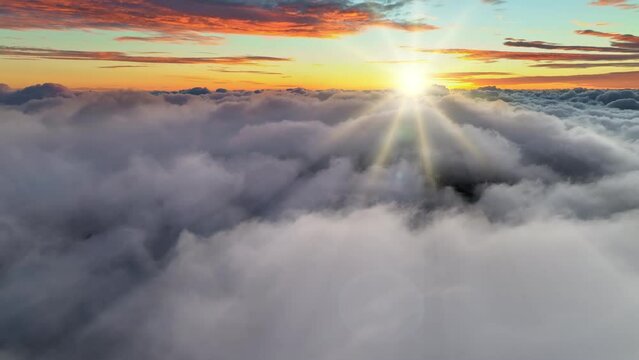 Breathtaking sunrise above the clouds. Aerial UHD shot of big puffy clouds and orange sky with rising sun. Sunrise in the mountains over fog and clounds