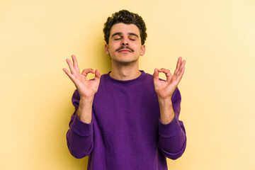Fototapeta premium Young caucasian man isolated on yellow background relaxes after hard working day, she is performing yoga.