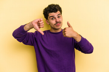 Fototapeta premium Young caucasian man isolated on yellow background showing thumbs up and thumbs down, difficult choose concept