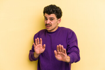 Young caucasian man isolated on yellow background rejecting someone showing a gesture of disgust.