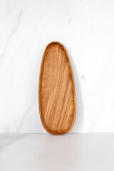Wooden oval oak dish, board, tray standing near the wall. Empty wooden plate on kitchen white table. Empty and template mockup with place for food. Kitchen utensils.