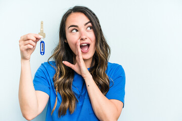 Young caucasian woman holding home keys isolated on blue background is saying a secret hot braking news and looking aside