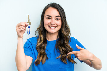 Young caucasian woman holding home keys isolated on blue background person pointing by hand to a shirt copy space, proud and confident