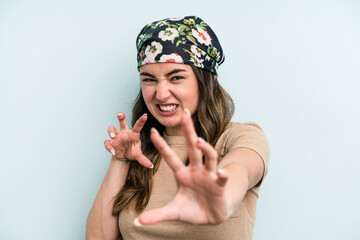 Young caucasian woman isolated on blue background showing claws imitating a cat, aggressive gesture.