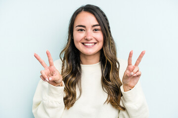 Young caucasian woman isolated on blue background showing victory sign and smiling broadly.