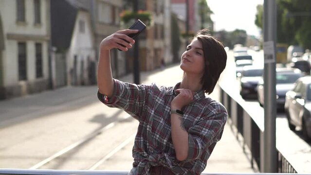 Young woman taking photos of herself with smartphone at the street on bright sunny day