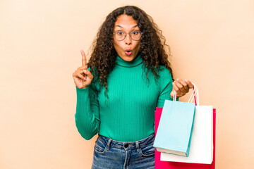 Young hispanic woman shopping some clothes isolated on beige background having some great idea, concept of creativity.