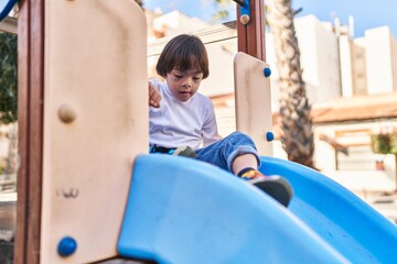 Fototapeta na wymiar Down syndrome kid playing on slide at park