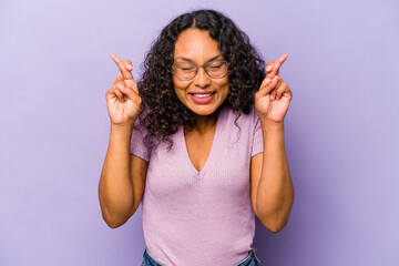 Young hispanic woman isolated on purple background crossing fingers for having luck