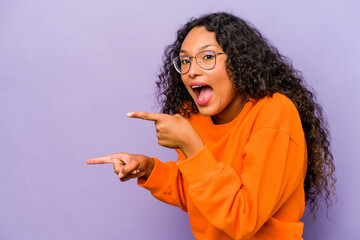 Young hispanic woman isolated on purple background excited pointing with forefingers away.