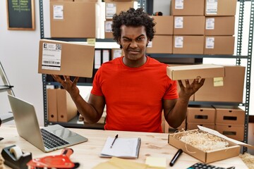 African man with curly hair working at small business ecommerce winking looking at the camera with sexy expression, cheerful and happy face.