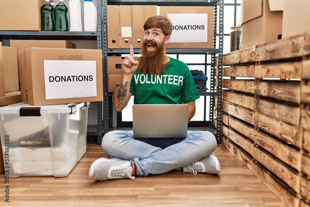 Sticker Caucasian man with long beard wearing volunteer t shirt using laptop surprised with an idea or question pointing finger with happy face, number one