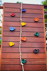 Artificial rock climbing wall. Wooden wall with rope and artificial rock for kids climbing. Playground equipment for children activity. 