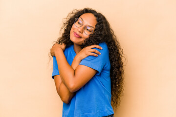 Young hispanic woman isolated on beige background hugs, smiling carefree and happy.